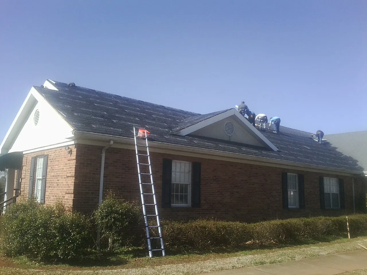 Crew tearing shingles off a brick ranch roof with a ladder set — Metal Roof Repair work by our crew in Neelyton