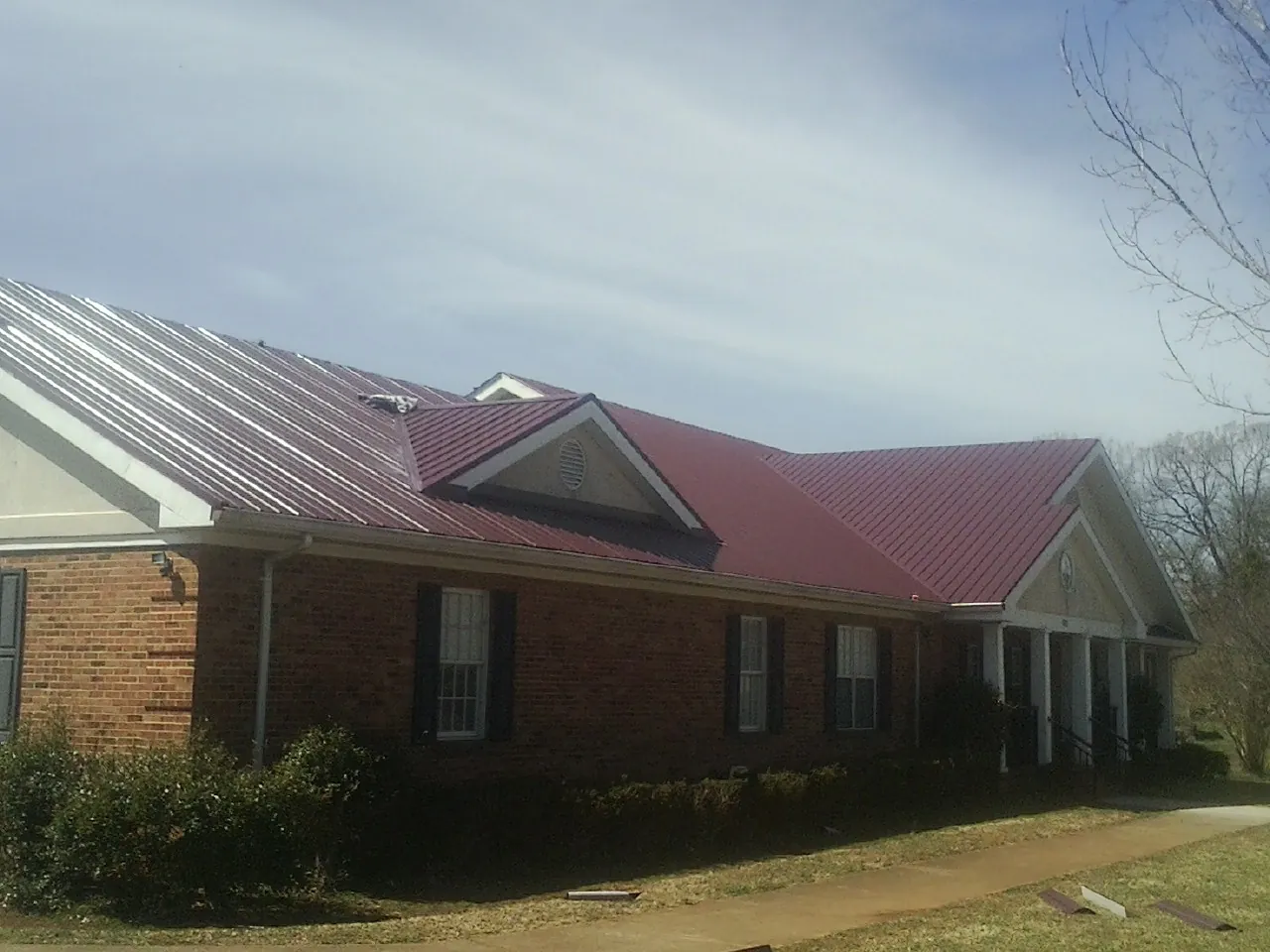 Red metal roof with gabled entries on a long brick building, from a Hail Damage Roof Repair job in Neelyton
