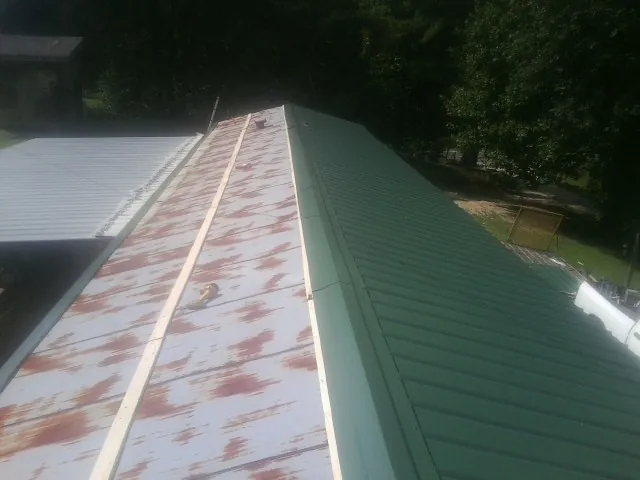 Old rusted panels beside newly installed green metal roofing — Wind Damage Roof Repair by Roofing Brothers in Neelyton