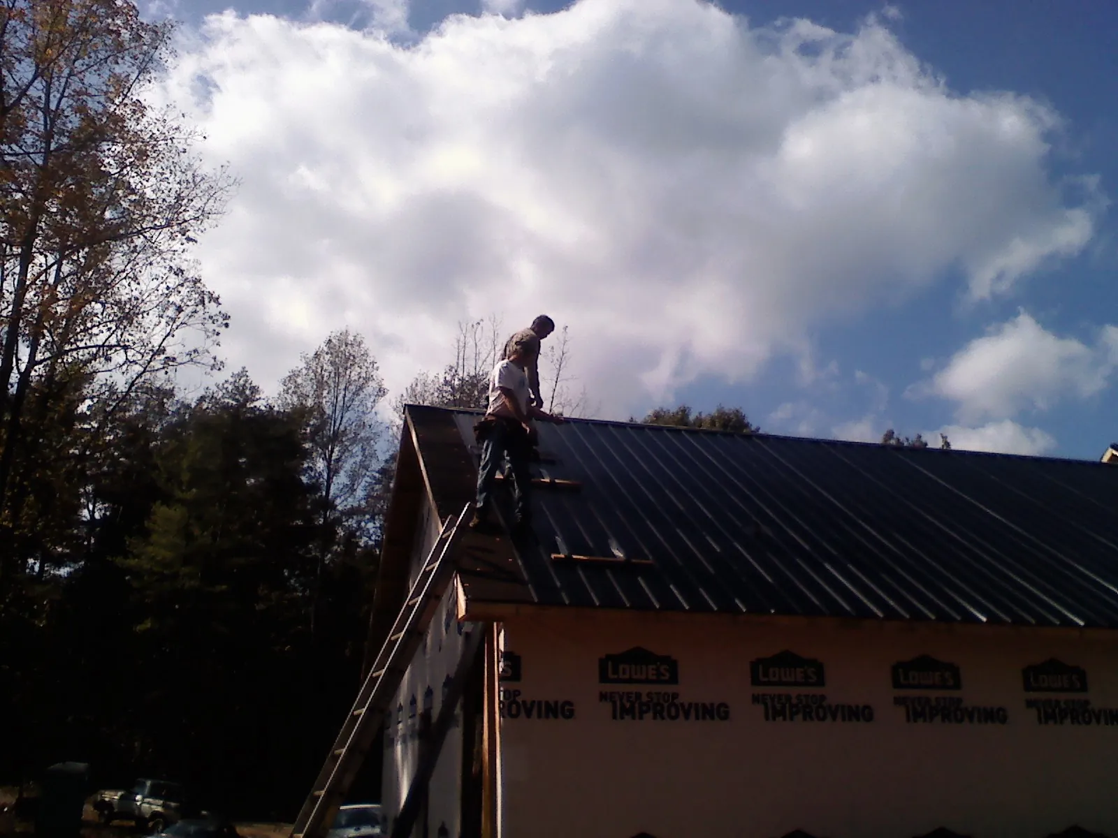 Roofer fastening dark metal panels high against a cloudy sky, from a Roof Inspection job in Neelyton