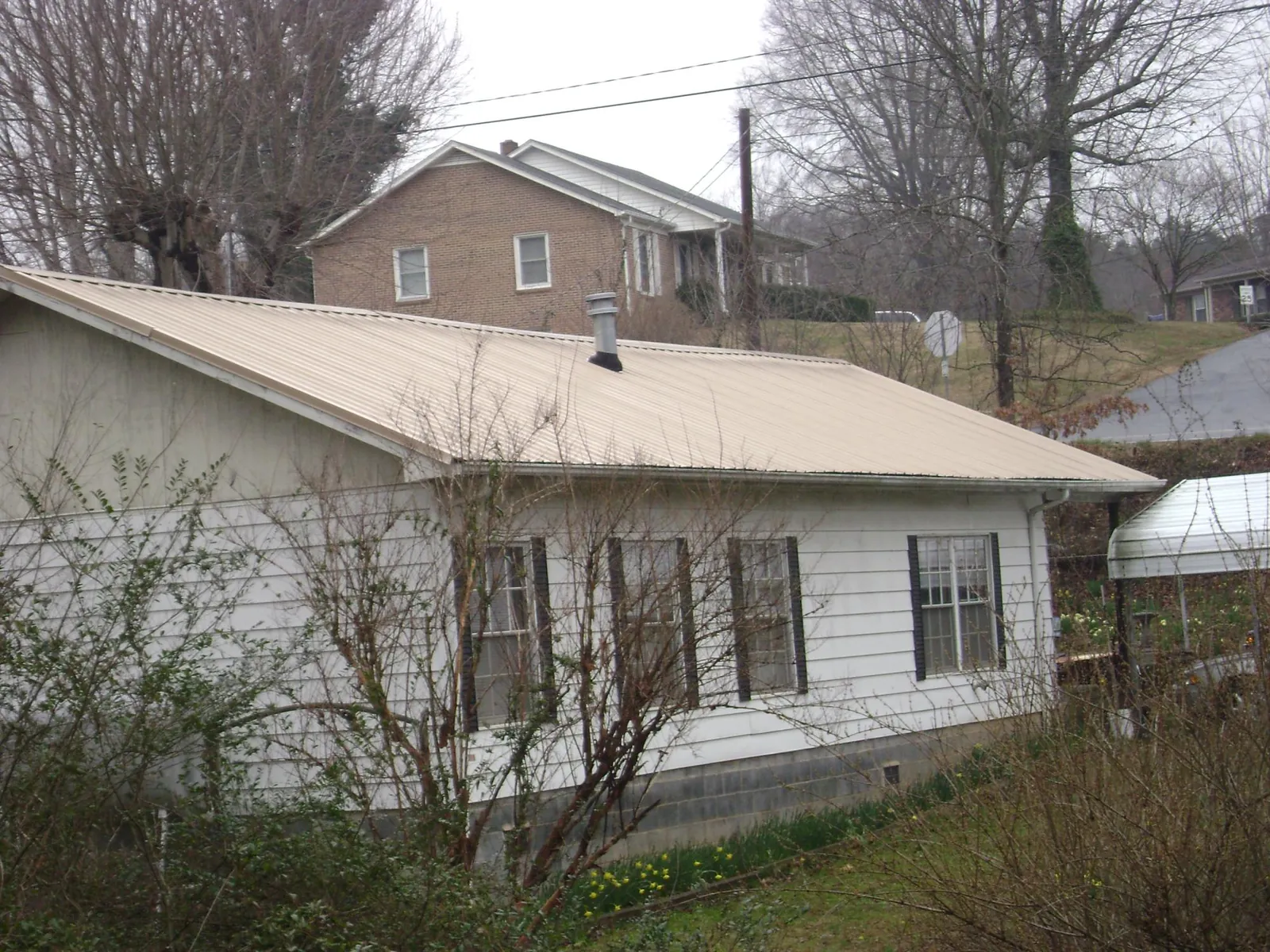 Tan metal roof on a white sided house set into a hillside — Commercial Roofing by Roofing Brothers in Neelyton