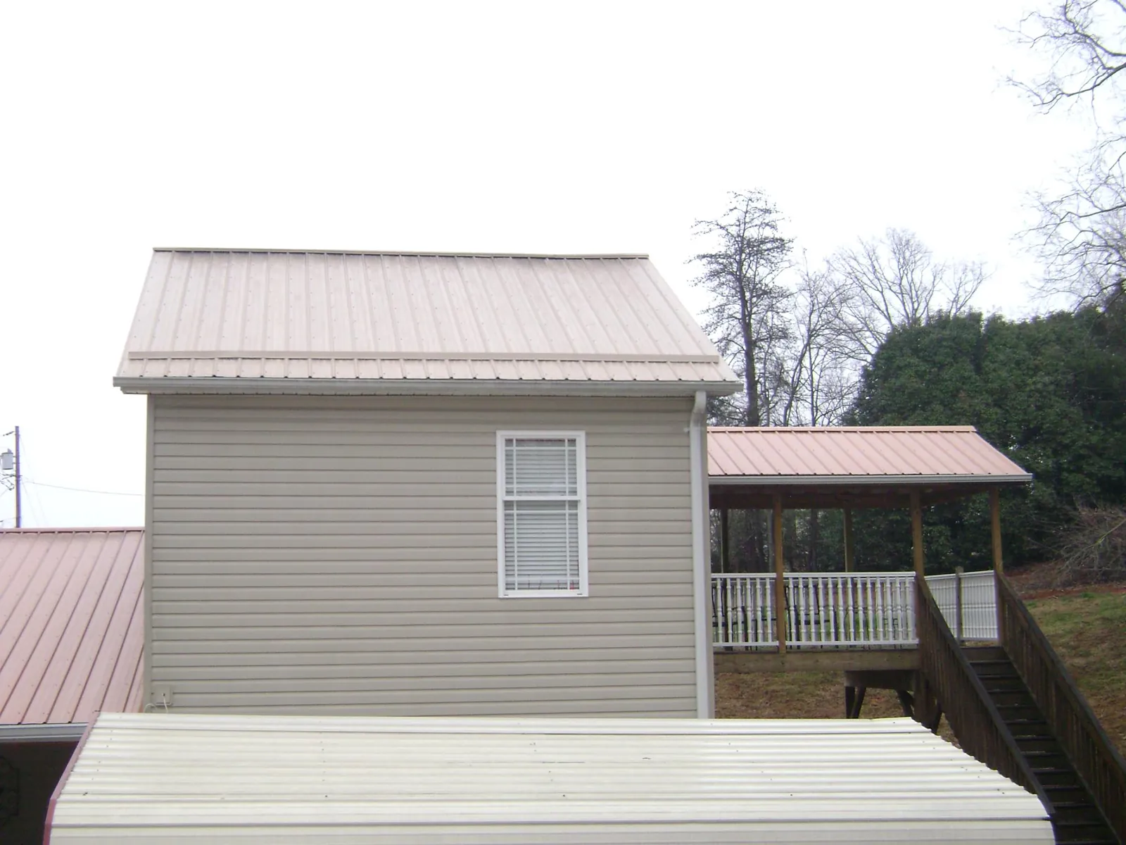 Tan metal roofs on a two story addition and attached porch, from a Roof Replacement job in Neelyton